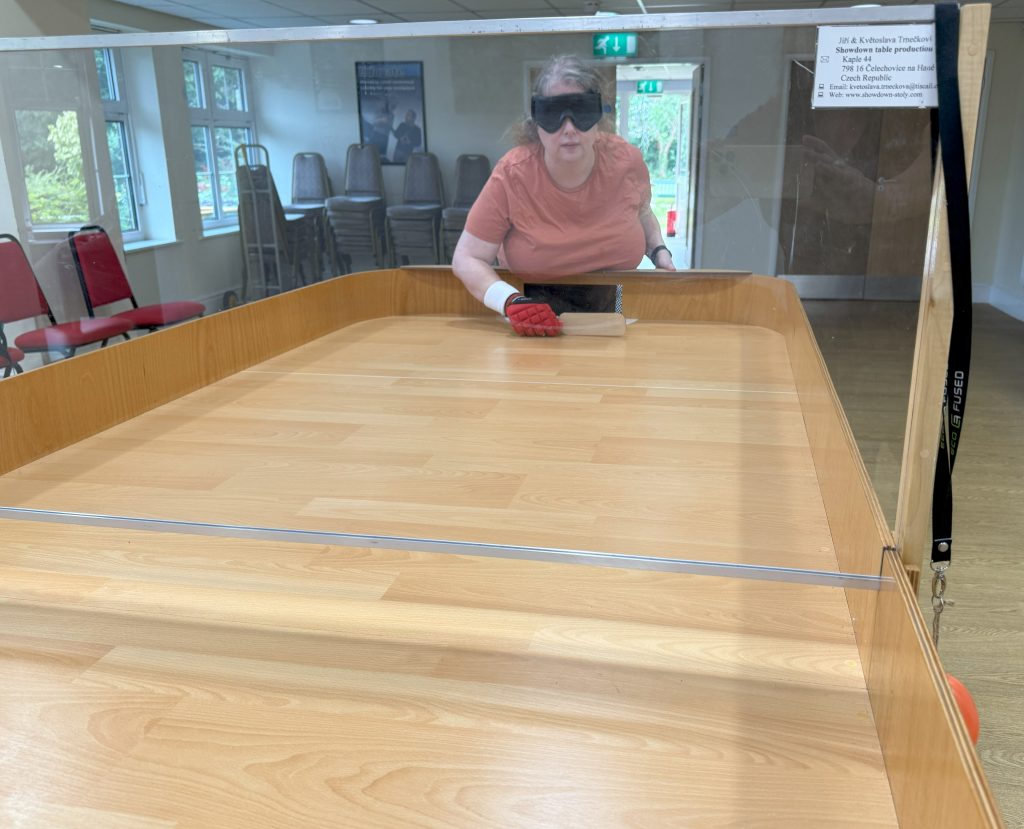 Shot looking along the full length of the table at Kara who is stood with her bat in a defensive position waiting for her opponent to serve.