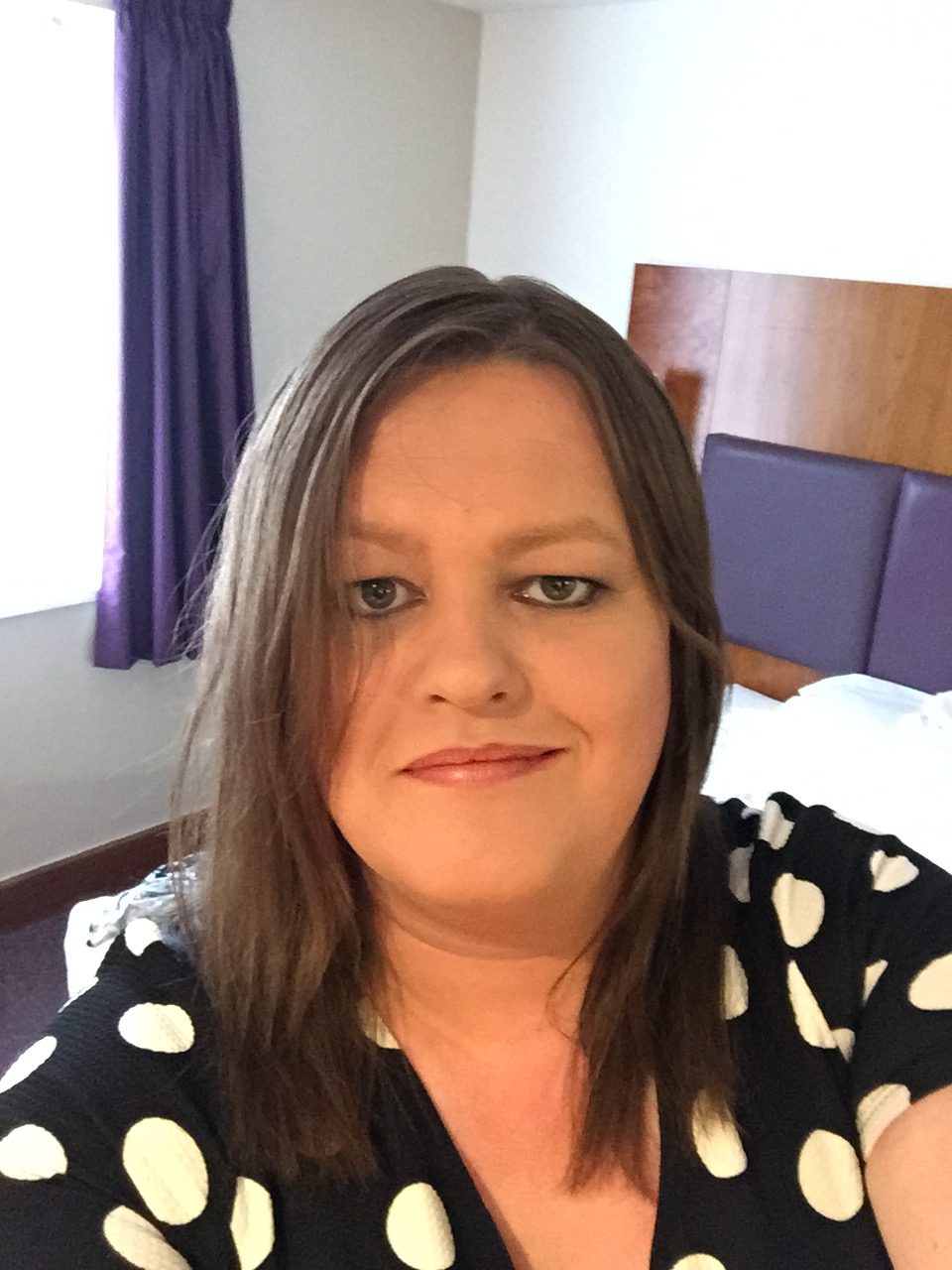 Photo of Louise, head coach of Bury Aces smiling at the camera, She has long dark hair and is wearing a black dress with white dots.